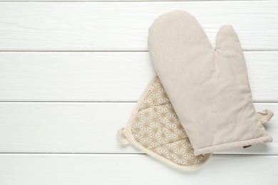 Photo of Oven glove and potholder on white wooden table, top view. Space for text