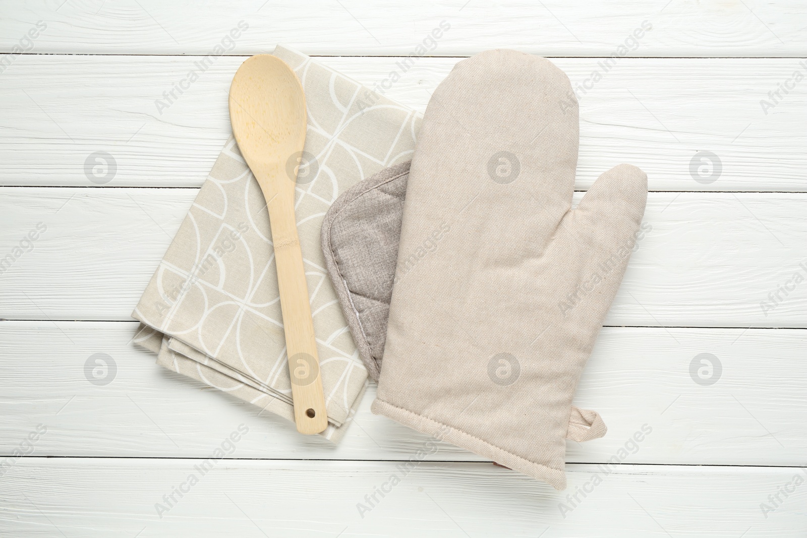 Photo of Oven glove, potholder, spoon and towel on white wooden table, top view
