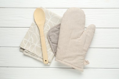 Photo of Oven glove, potholder, spoon and towel on white wooden table, top view