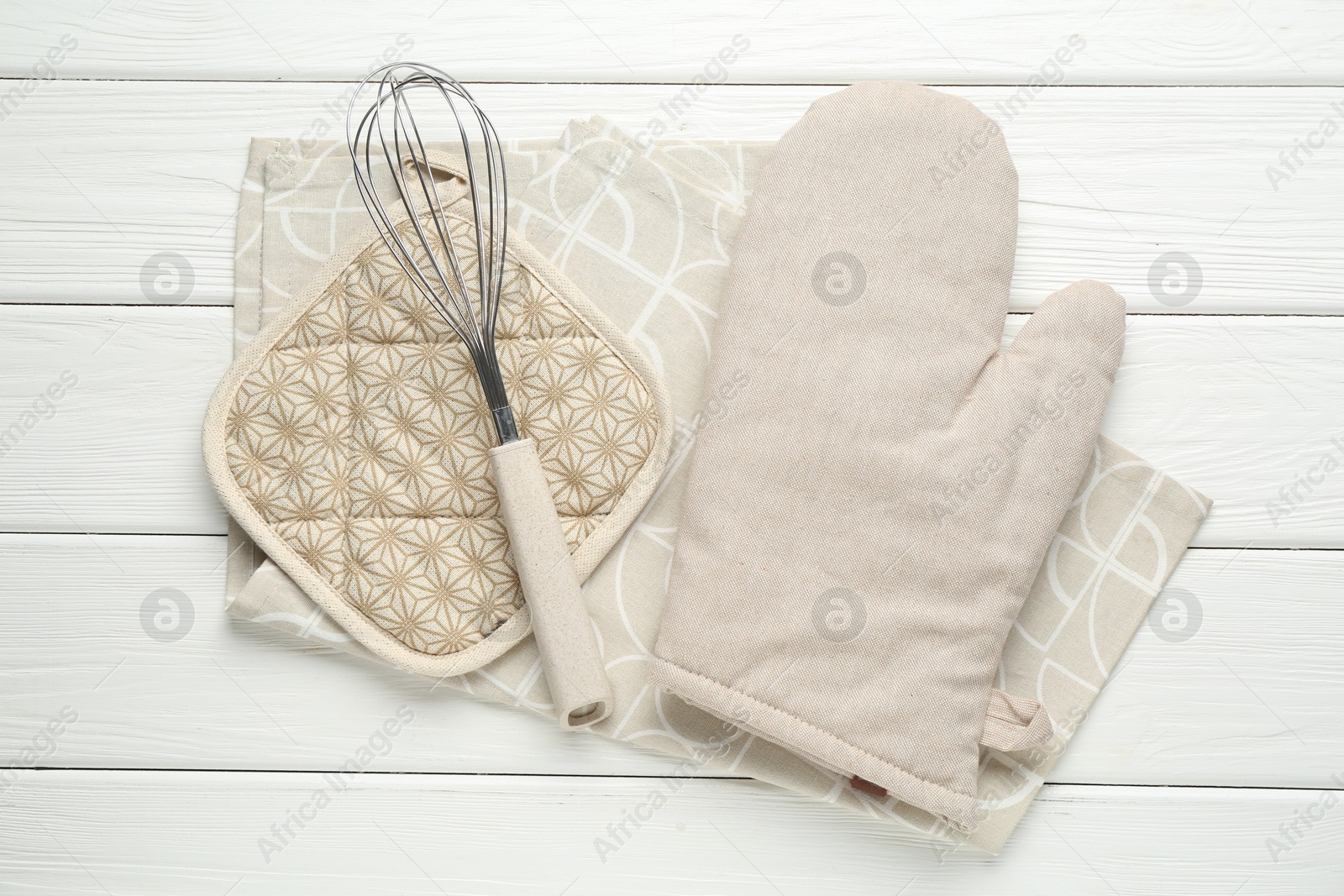 Oven glove, potholder, whisk and towel on white wooden table, flat lay Photo of Oven glove, potholder, whisk and towel on white wooden table, flat lay