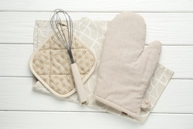 Photo of Oven glove, potholder, whisk and towel on white wooden table, flat lay