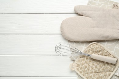 Photo of Oven glove, potholder, whisk and towel on white wooden table, flat lay. Space for text