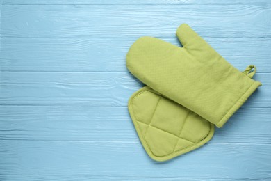 Photo of Green oven glove and potholder on light blue wooden table, flat lay. Space for text