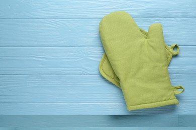 Photo of Green oven glove and potholder on light blue wooden table, top view. Space for text
