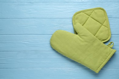Photo of Green oven glove and potholder on light blue wooden table, flat lay. Space for text
