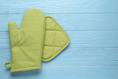 Photo of Green oven glove and potholder on light blue wooden table, flat lay. Space for text