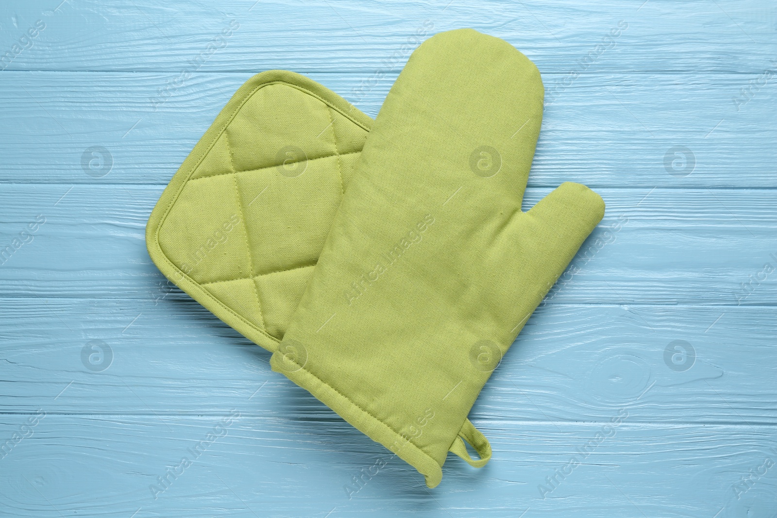 Photo of Green oven glove and potholder on light blue wooden table, top view