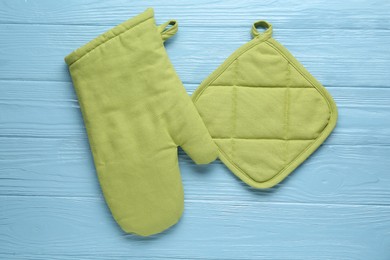Photo of Green oven glove and potholder on light blue wooden table, flat lay