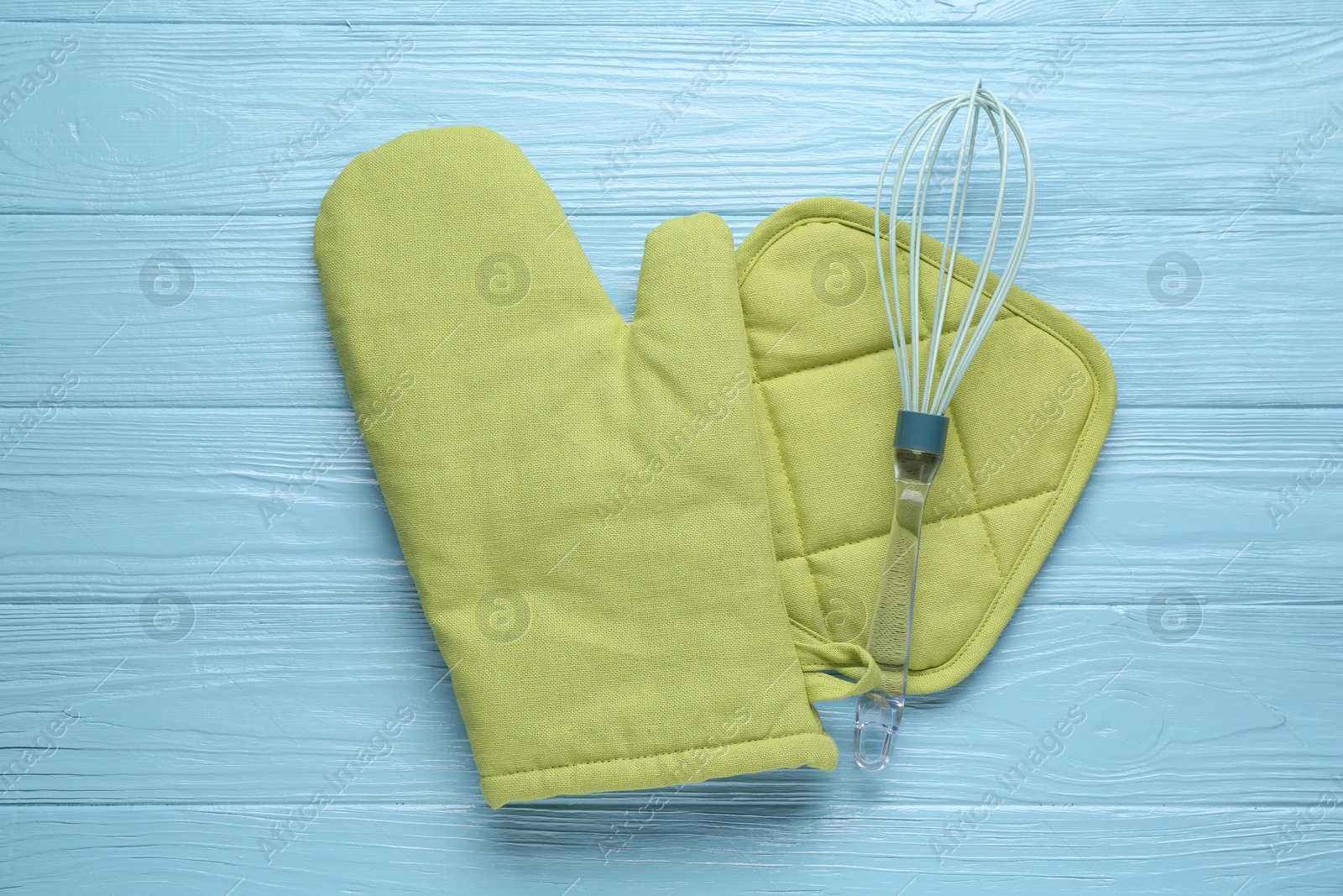 Photo of Green oven glove, potholder and whisk on light blue wooden table, flat lay