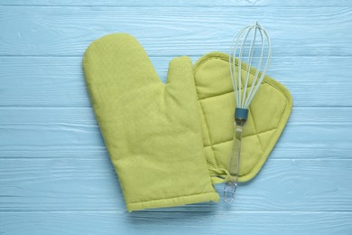 Photo of Green oven glove, potholder and whisk on light blue wooden table, flat lay