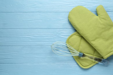 Photo of Green oven glove, potholder and whisk on light blue wooden table, flat lay. Space for text