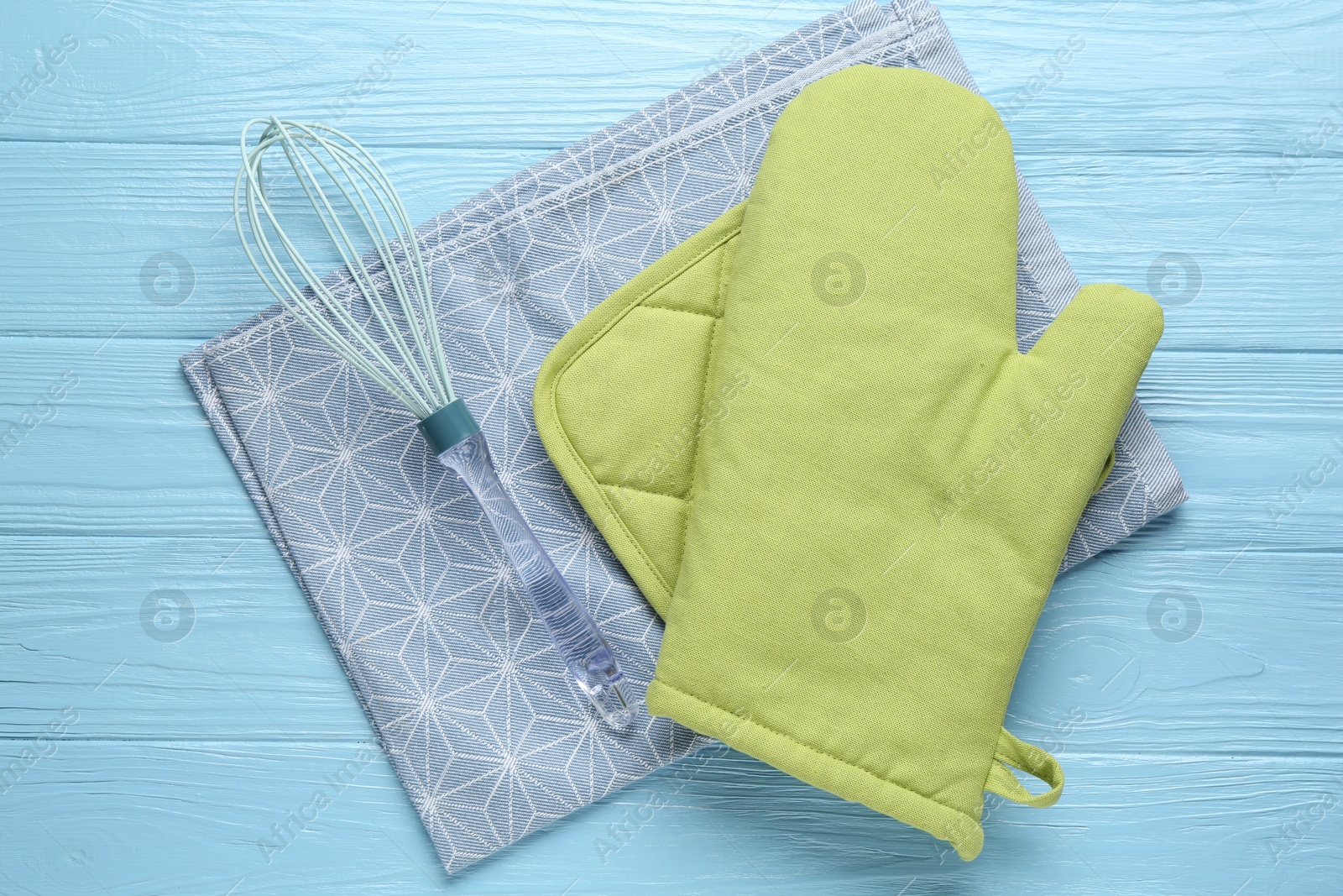 Photo of Green oven glove, potholder, towel and whisk on light blue wooden table, flat lay