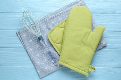 Photo of Green oven glove, potholder, towel and whisk on light blue wooden table, flat lay