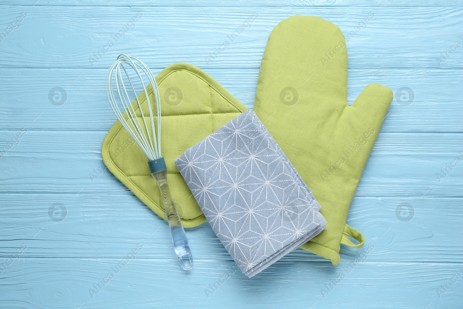 Green oven glove, potholder, towel and whisk on light blue wooden table, flat lay Photo of Green oven glove, potholder, towel and whisk on light blue wooden table, flat lay