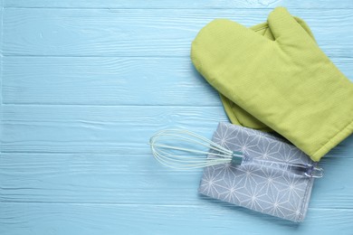 Photo of Green oven glove, potholder, towel and whisk on light blue wooden table, flat lay. Space for text