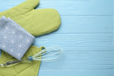 Photo of Green oven glove, potholder, towel and whisk on light blue wooden table, flat lay. Space for text