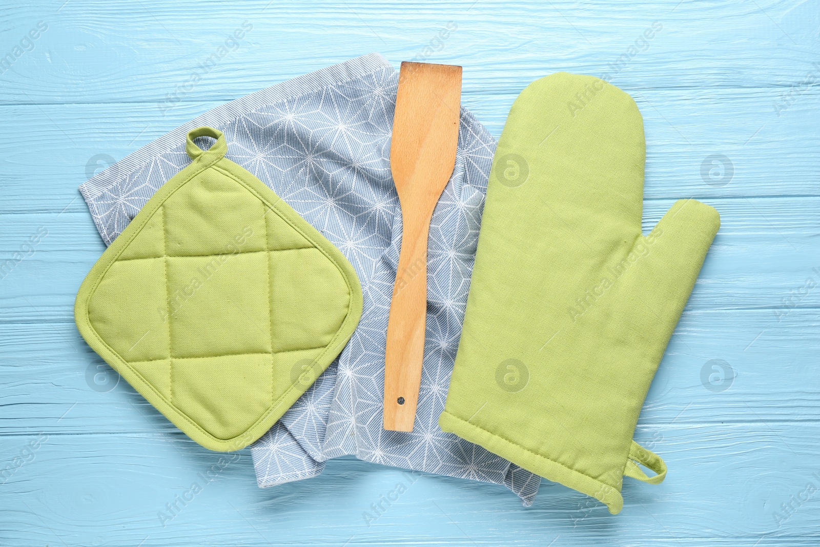 Green oven glove, potholder, towel and spatula on light blue wooden table, flat lay Photo of Green oven glove, potholder, towel and spatula on light blue wooden table, flat lay
