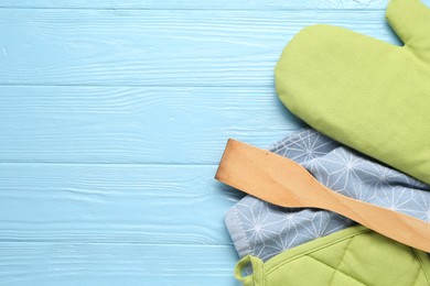 Photo of Green oven glove, potholder, towel and spatula on light blue wooden table, flat lay. Space for text