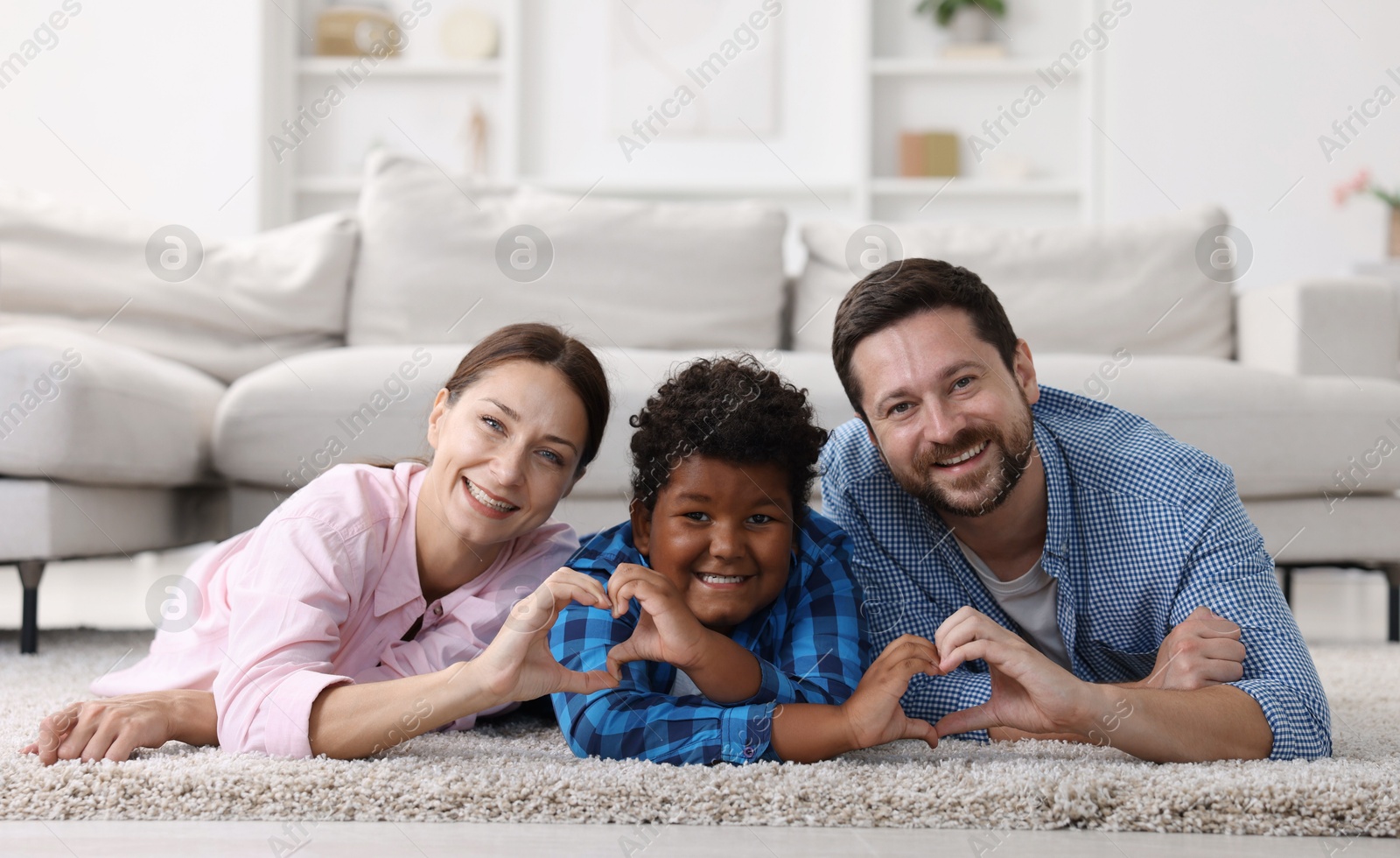 Photo of Adoption. Parents and their son making heart gestures on floor at home