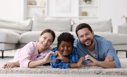 Photo of Adoption. Parents and their son making heart gestures on floor at home