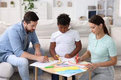 Photo of Adoption. Parents and their son drawing together at table indoors