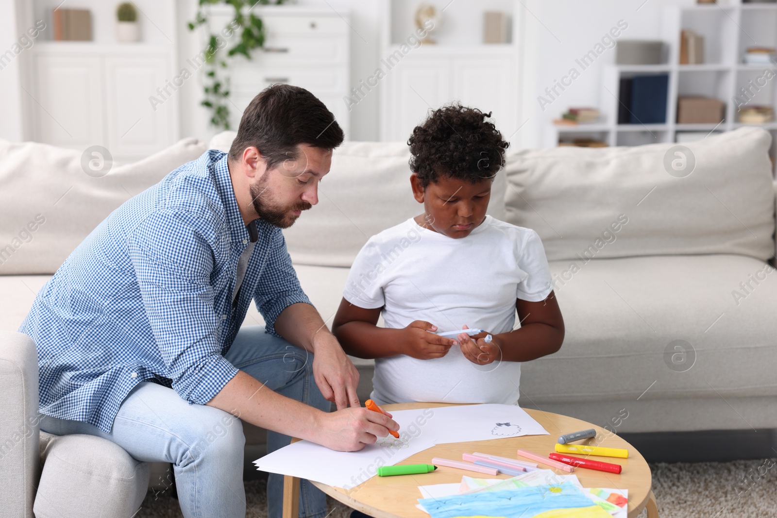 Photo of Adoption. Father and his son drawing together at table indoors