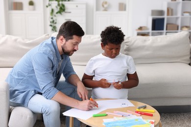 Photo of Adoption. Father and his son drawing together at table indoors