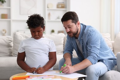 Photo of Adoption. Father and his son drawing together at table indoors