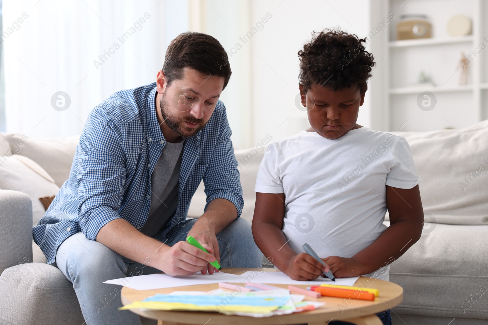 Adoption. Father and his son drawing together at table indoors Photo of Adoption. Father and his son drawing together at table indoors