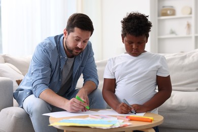 Photo of Adoption. Father and his son drawing together at table indoors