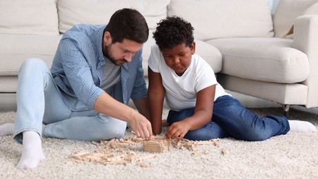 Photo of Adoption. Father and his son playing with wooden blocks on floor at home
