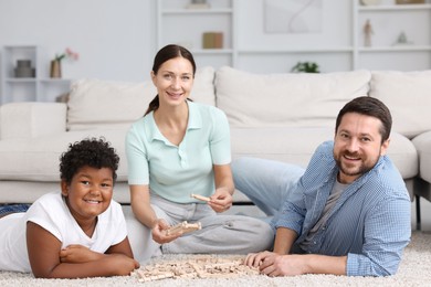 Photo of Adoption. Parents and their son playing with wooden blocks on floor at home