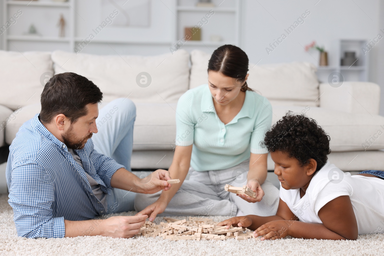 Photo of Adoption. Parents and their son playing with wooden blocks on floor at home