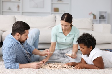 Photo of Adoption. Parents and their son playing with wooden blocks on floor at home