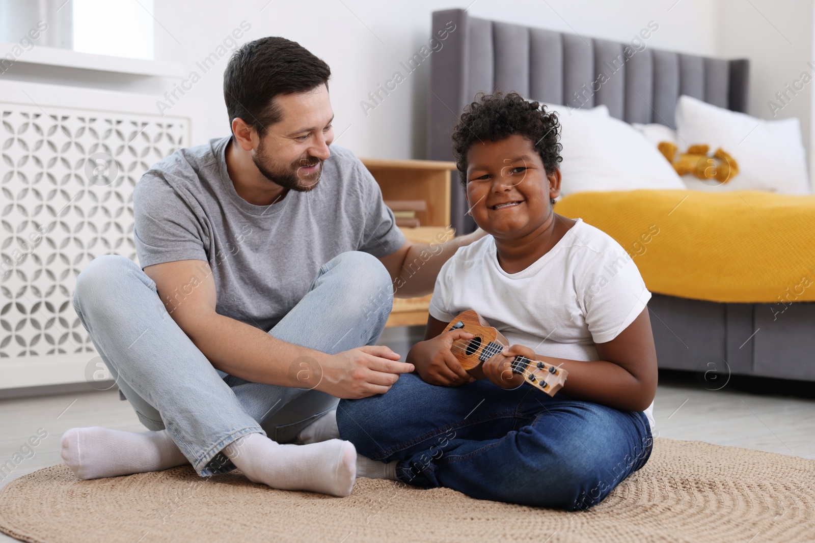 Photo of Adoption. Father teaching his son to play ukulele on floor at home