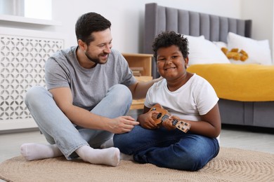 Photo of Adoption. Father teaching his son to play ukulele on floor at home