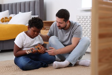 Photo of Adoption. Father teaching his son to play ukulele on floor at home