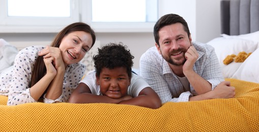 Photo of Adoption. Happy parents and their son on bed at home
