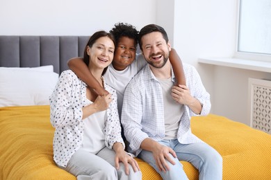 Photo of Adoption. Happy parents and their son on bed at home
