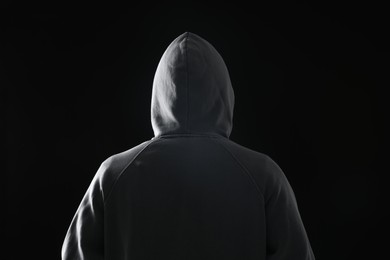 Photo of Criminal in hood on dark background, back view