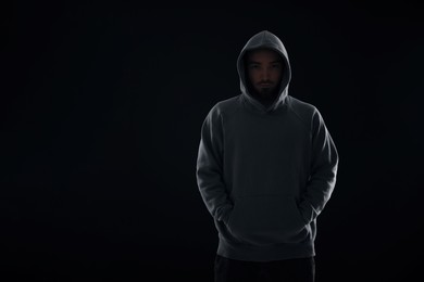 Photo of Criminal man in hood on dark background. Space for text