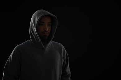 Photo of Criminal man in hood on dark background. Space for text