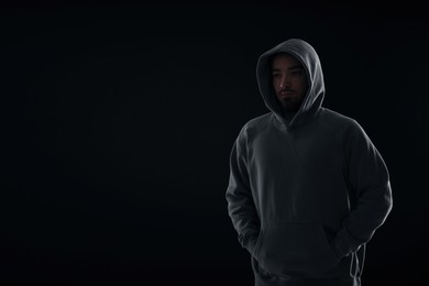 Photo of Criminal man in hood on dark background. Space for text