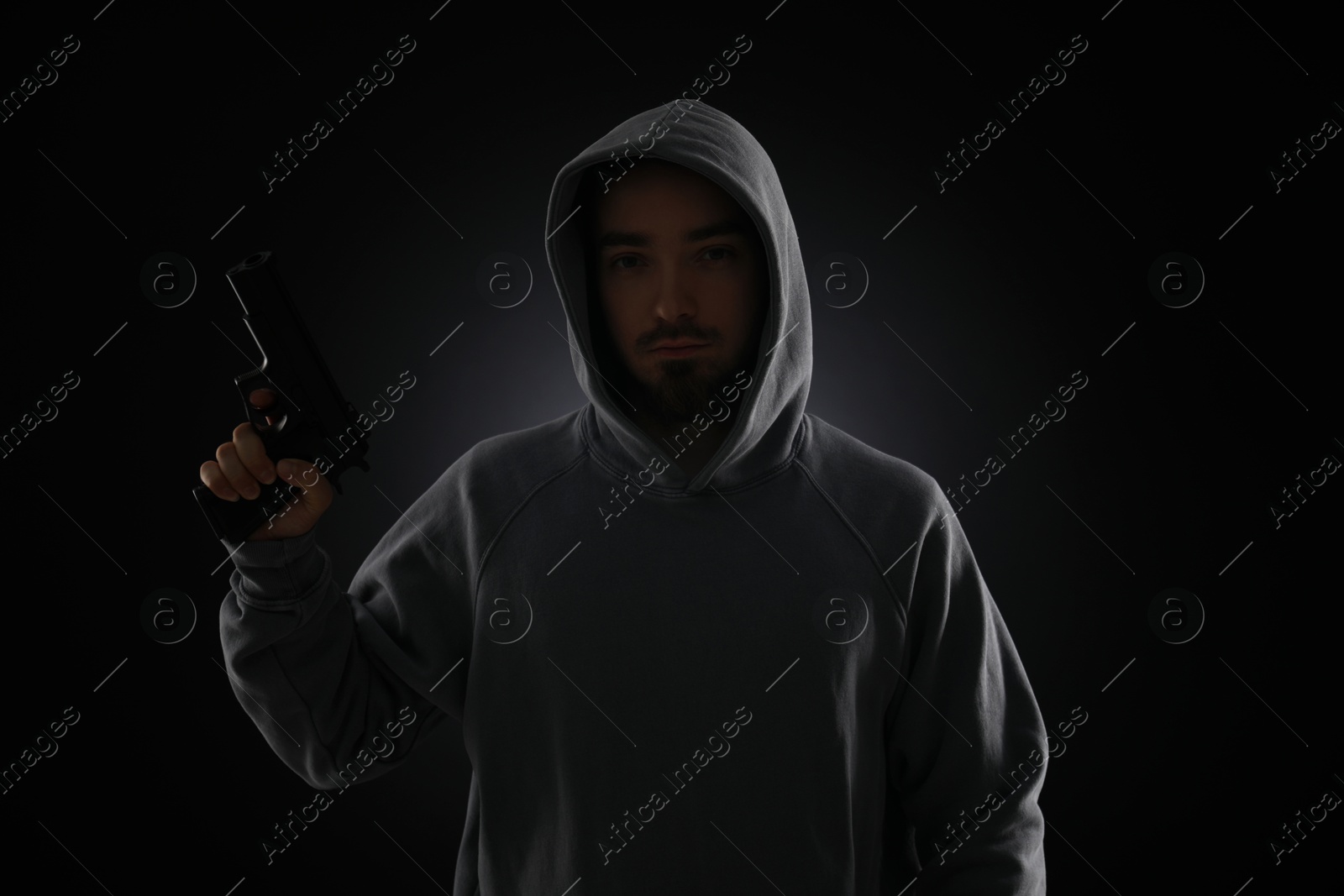 Criminal in hood with gun on dark background Photo of Criminal in hood with gun on dark background
