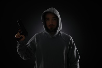 Photo of Criminal in hood with gun on dark background