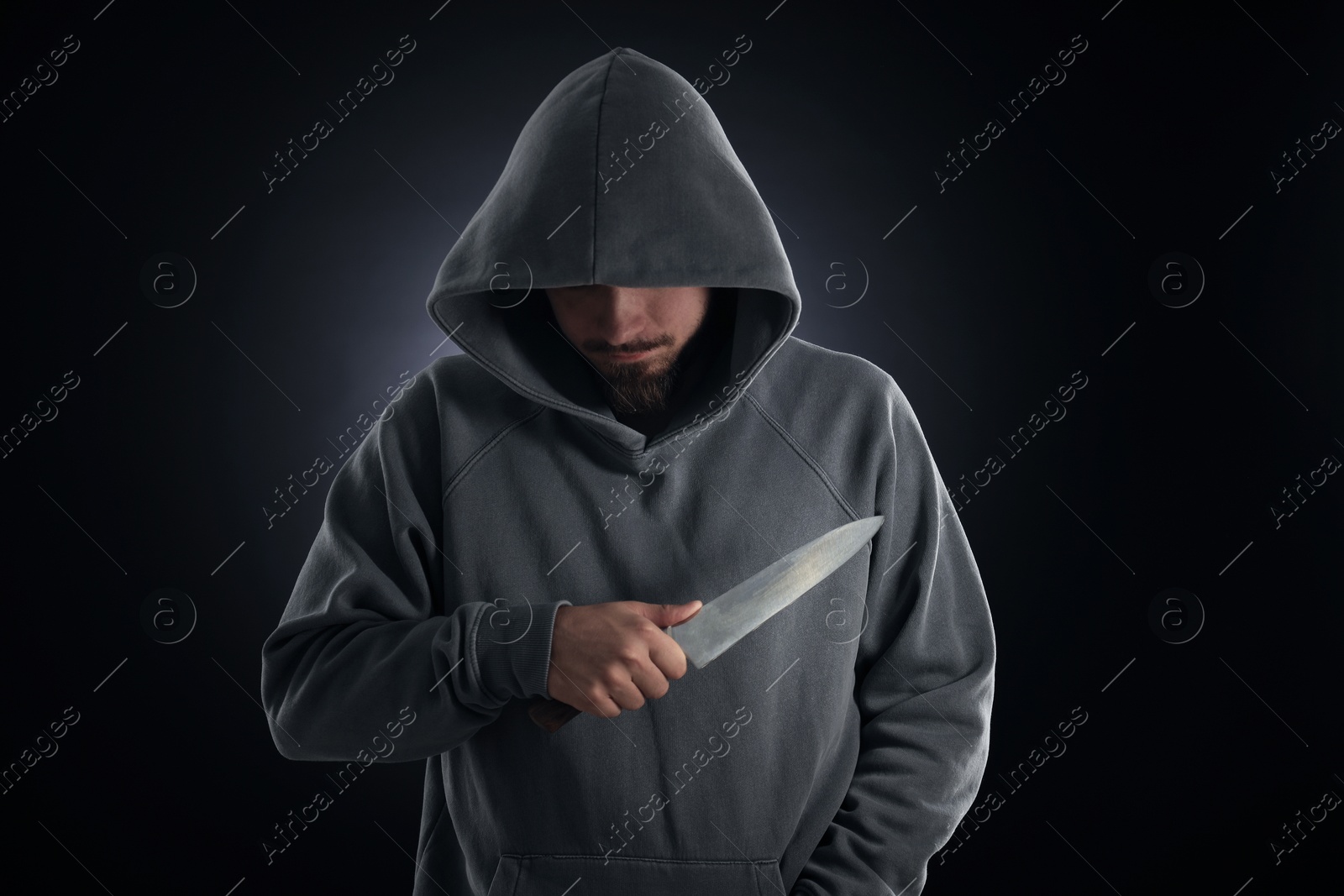 Criminal in hood with knife on dark background Photo of Criminal in hood with knife on dark background