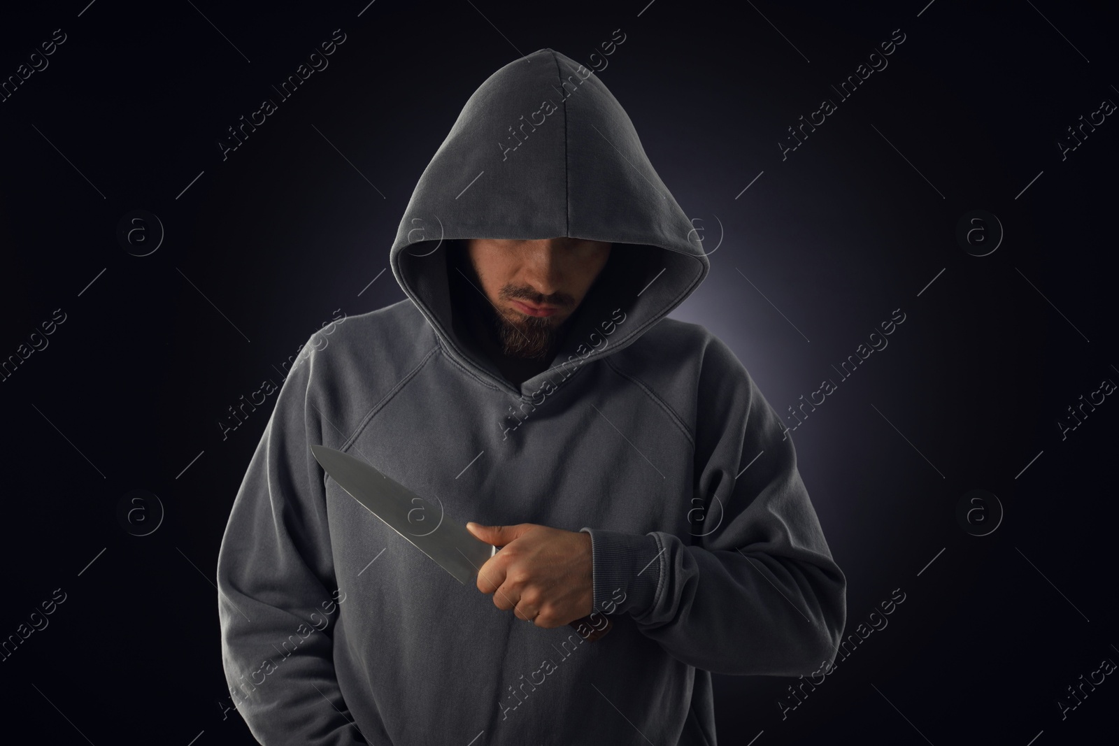 Criminal in hood with knife on dark background Photo of Criminal in hood with knife on dark background