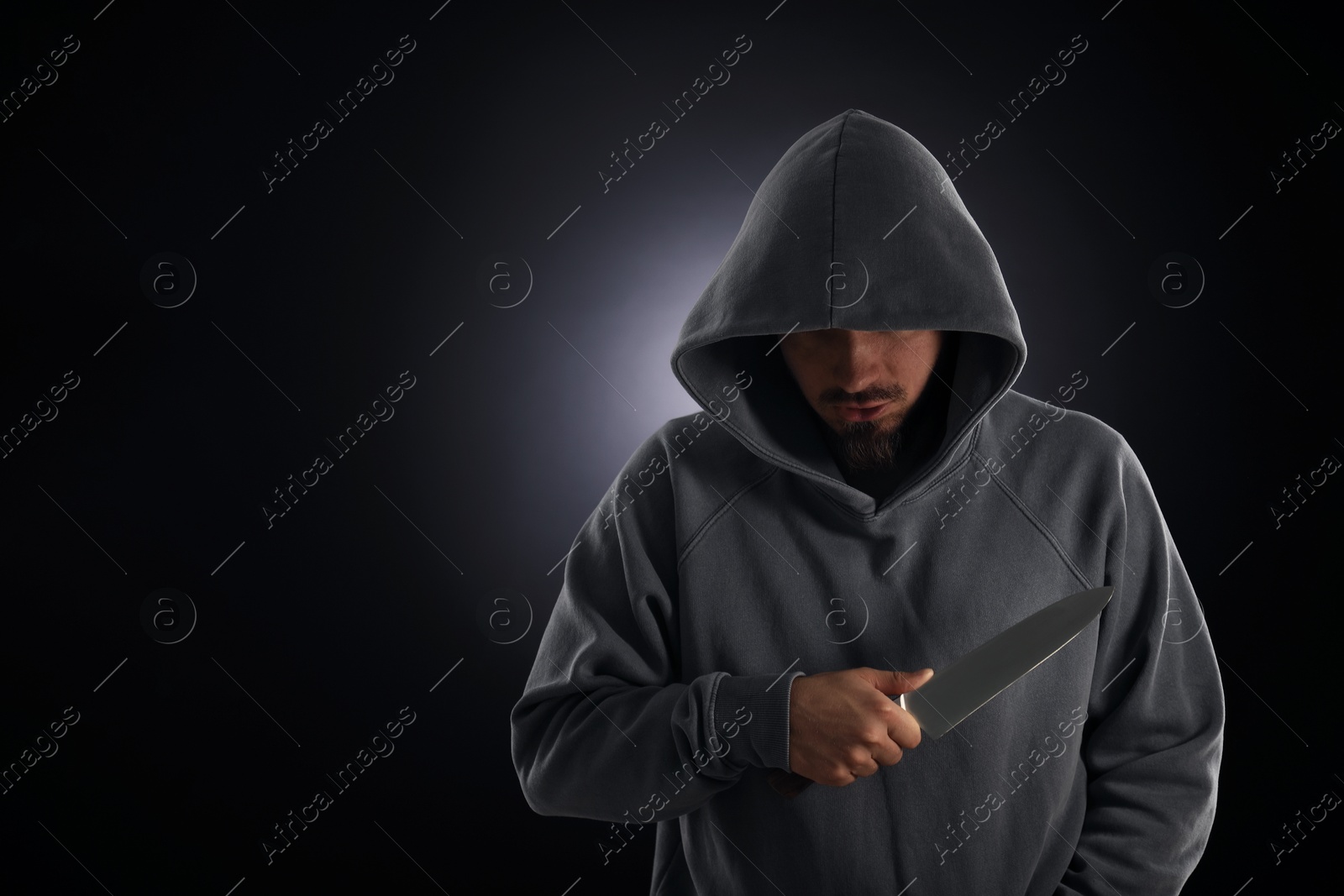 Criminal in hood with knife on dark background. Space for text Photo of Criminal in hood with knife on dark background. Space for text