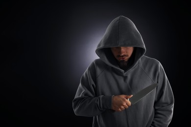 Photo of Criminal in hood with knife on dark background. Space for text
