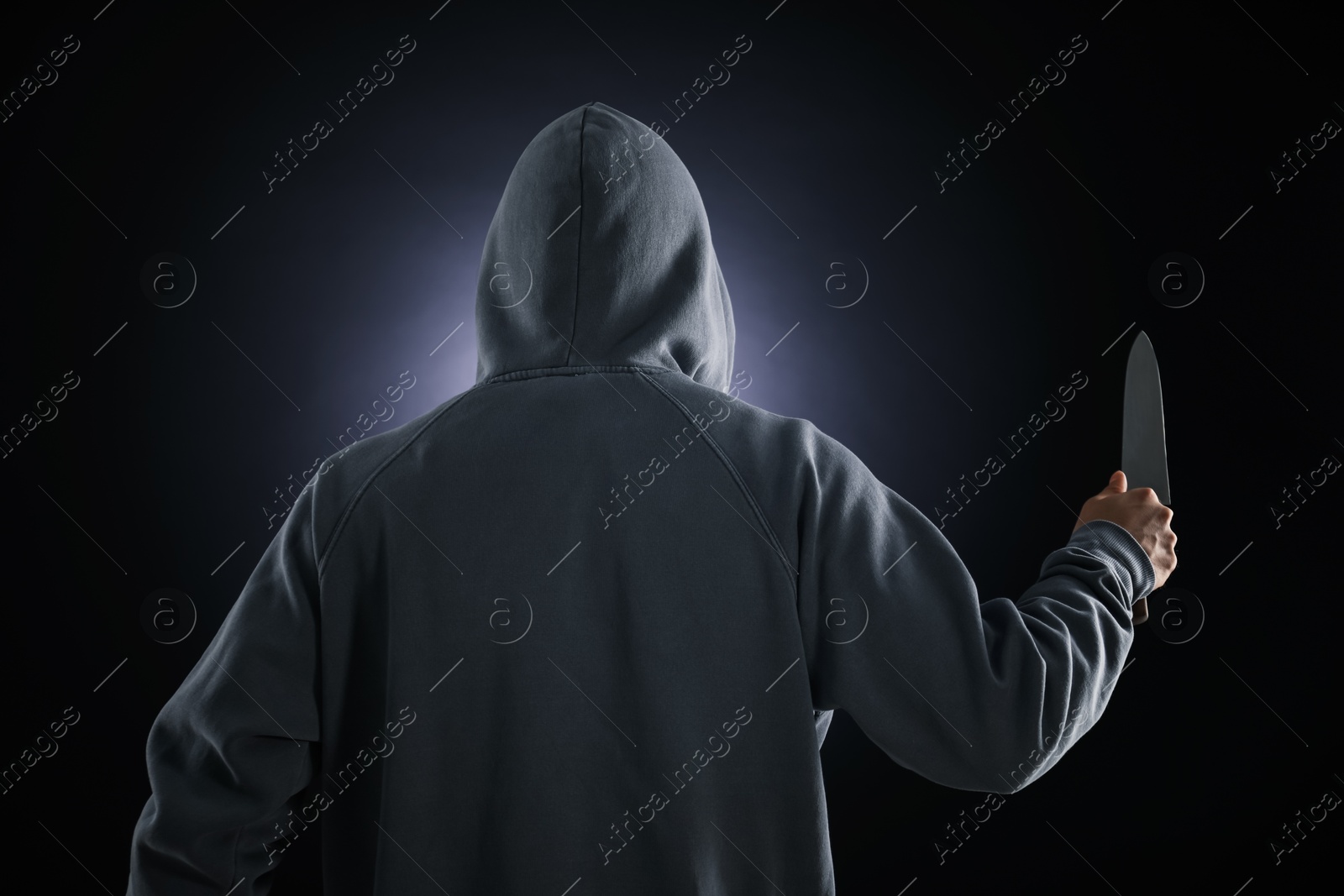 Criminal with knife on dark background, back view Photo of Criminal with knife on dark background, back view